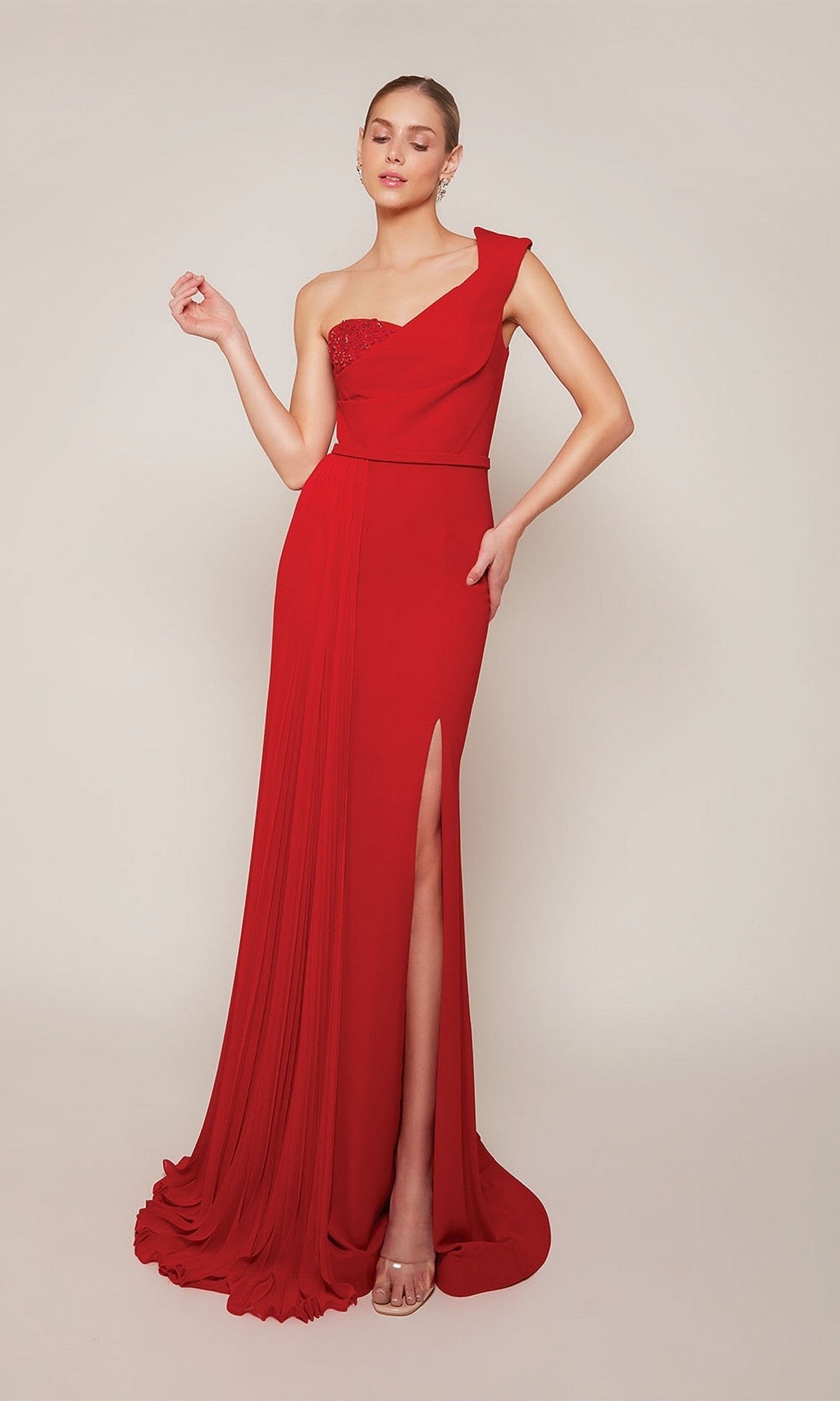 A woman poses gracefully in a red Alyce 27650 long formal dress, featuring a one-shoulder design, floor-length sheath silhouette, and thigh-high slit, set against a light background.
